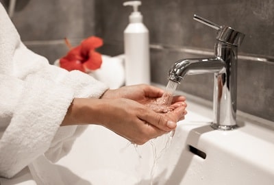 woman-in-robe-washes-her-hands-under-running-water-from-tap-min